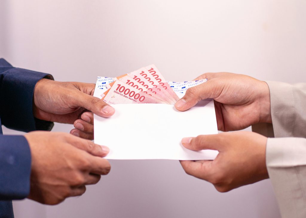pexels-photo-31679223-31679223 Hands exchanging an envelope with Indonesian Rupiah, highlighting financial transactions.